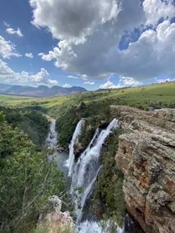 Cachoeira dupla caindo num cânion, com montanhas ao fundo