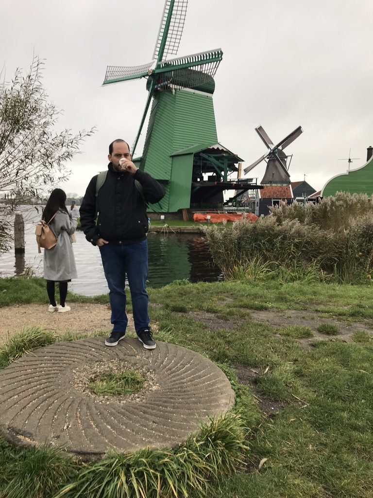 Tiago Lopes tomando café diante de moinhos verdes em Zaanse Schans