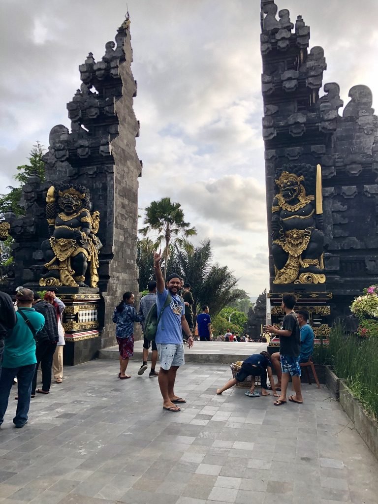 Tiago Lopes em frente ao portal de um templo balinês, com estátuas guardiãs