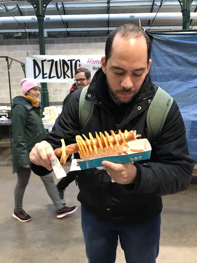 Tiago Lopes segurando uma batata em espiral em um mercado coberto