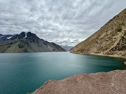 Lago de água turquesa entre montanhas áridas e nevadas, o Embalse El Yeso