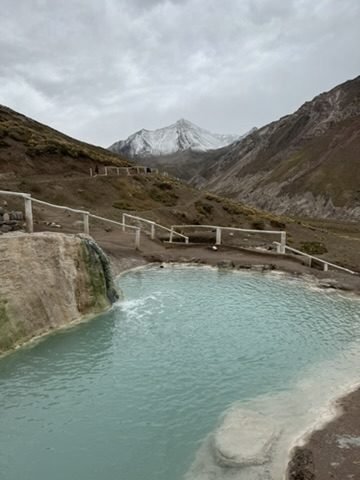 Piscina natural de águas termais azul-leitosas com montanha nevada ao fundo