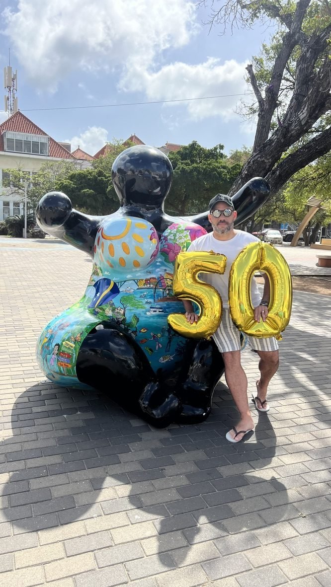 Tiago Lopes ao lado de uma escultura Chichi colorida segurando balões com o número 50