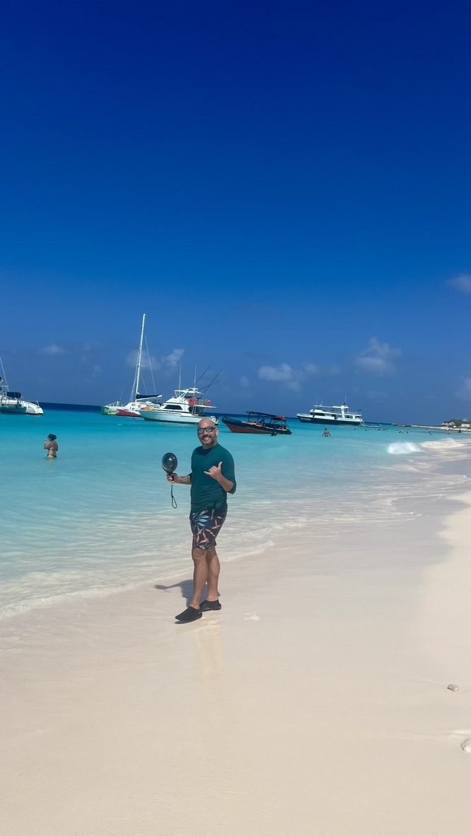 Tiago Lopes numa praia de areia branca com barcos ancorados