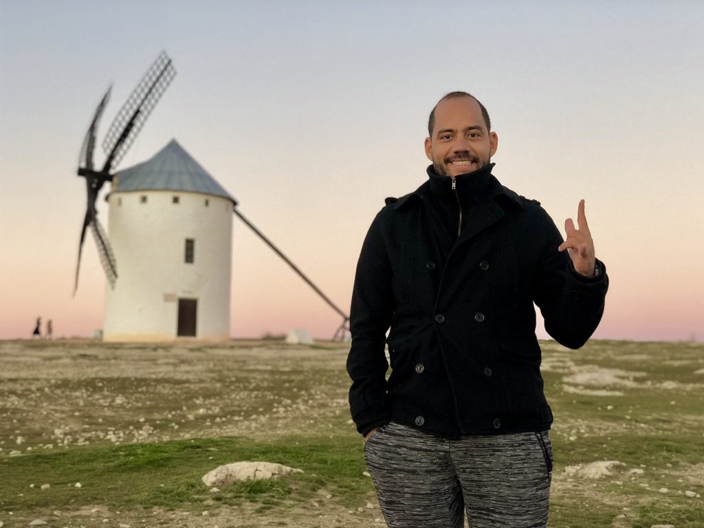 Tiago Lopes sorrindo diante de um moinho de vento branco ao entardecer, em La Mancha