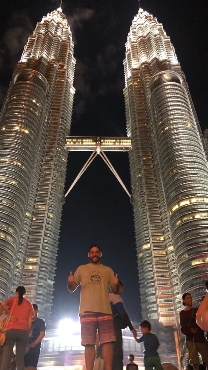 Tiago Lopes à noite diante das Torres Petronas iluminadas