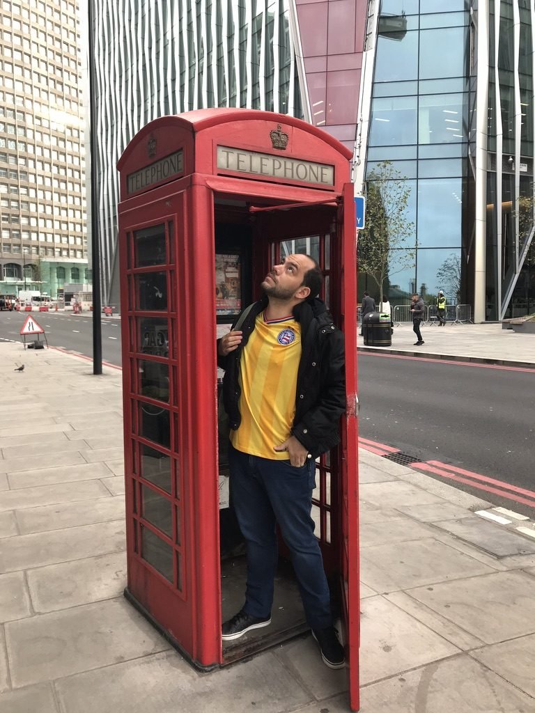 Tiago Lopes dentro de uma cabine telefônica vermelha, com a camisa do Bahia