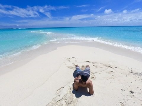 Tiago Lopes deitado na areia branca, com o mar turquesa ao fundo
