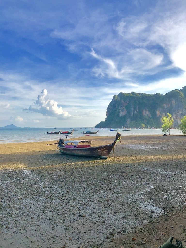 Barco long-tail na areia, com falésias de calcário ao fundo
